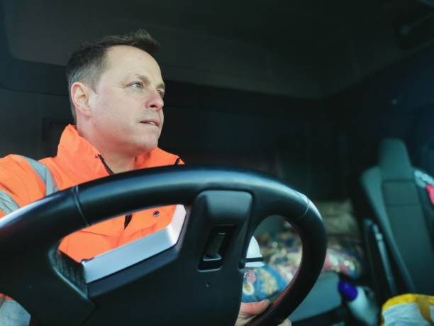 Middle Aged Male Truck Driver Wearing a High Visibility Jacket and holding the Vehicle Steering Wheel.
For educational purposes only