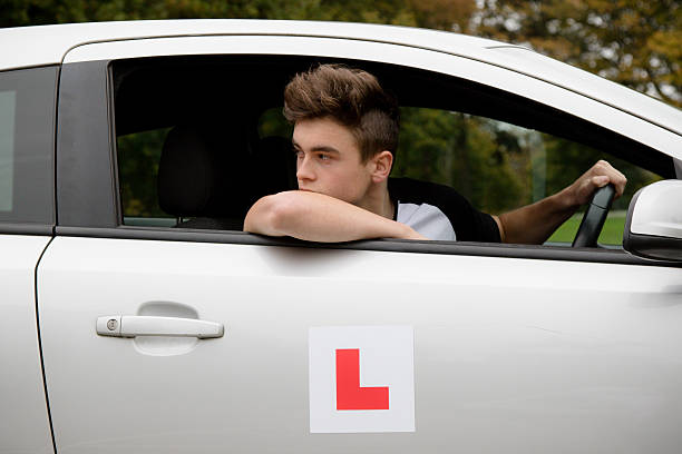 Teenage boy sitting in the drivers seat of a right hand drive car reversing.